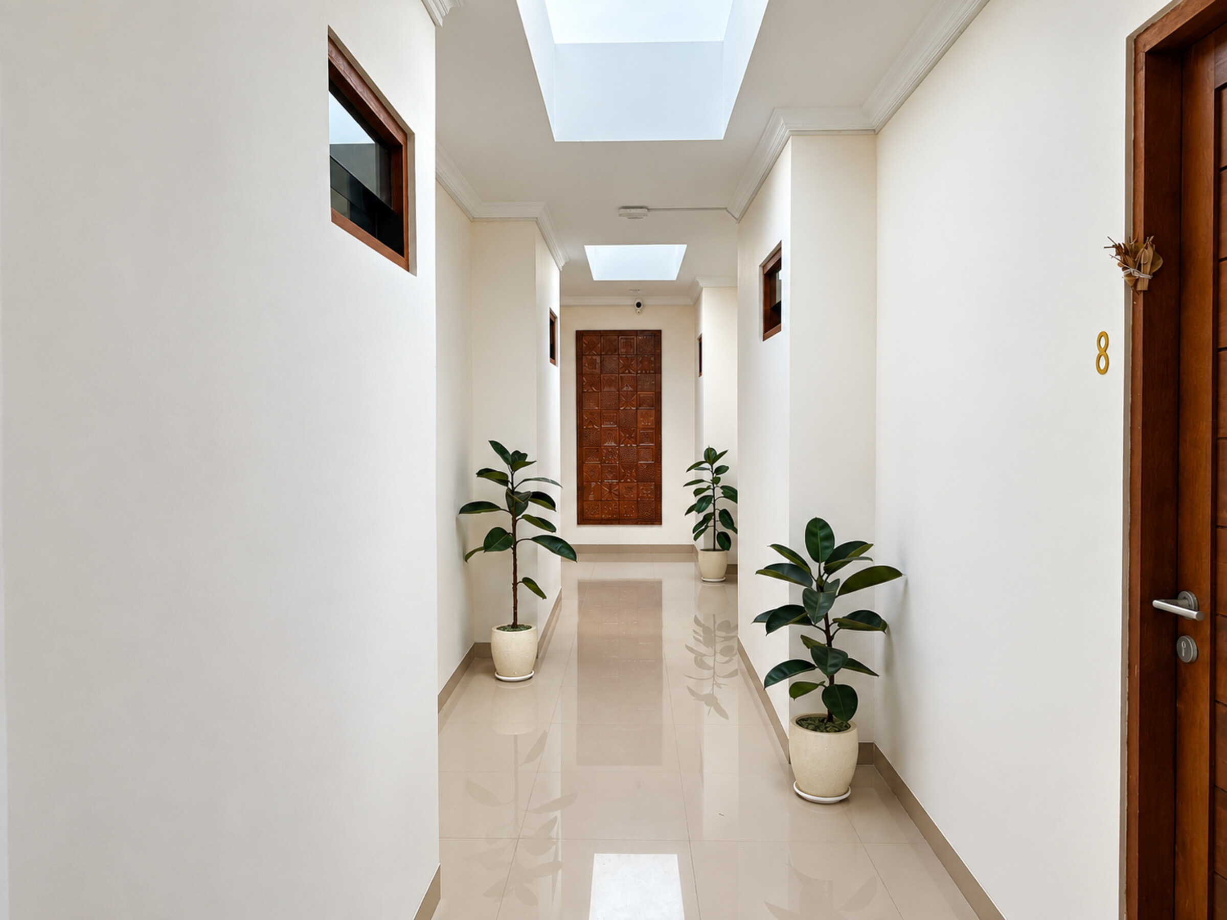 Bright corridor with skylights, wooden room doors and potted plants