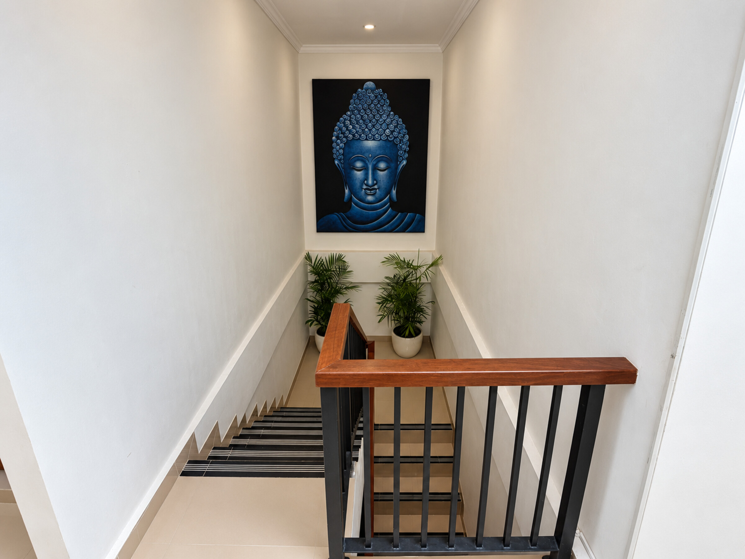 Staircase with a wooden handrail, potted palms and a blue Buddha painting